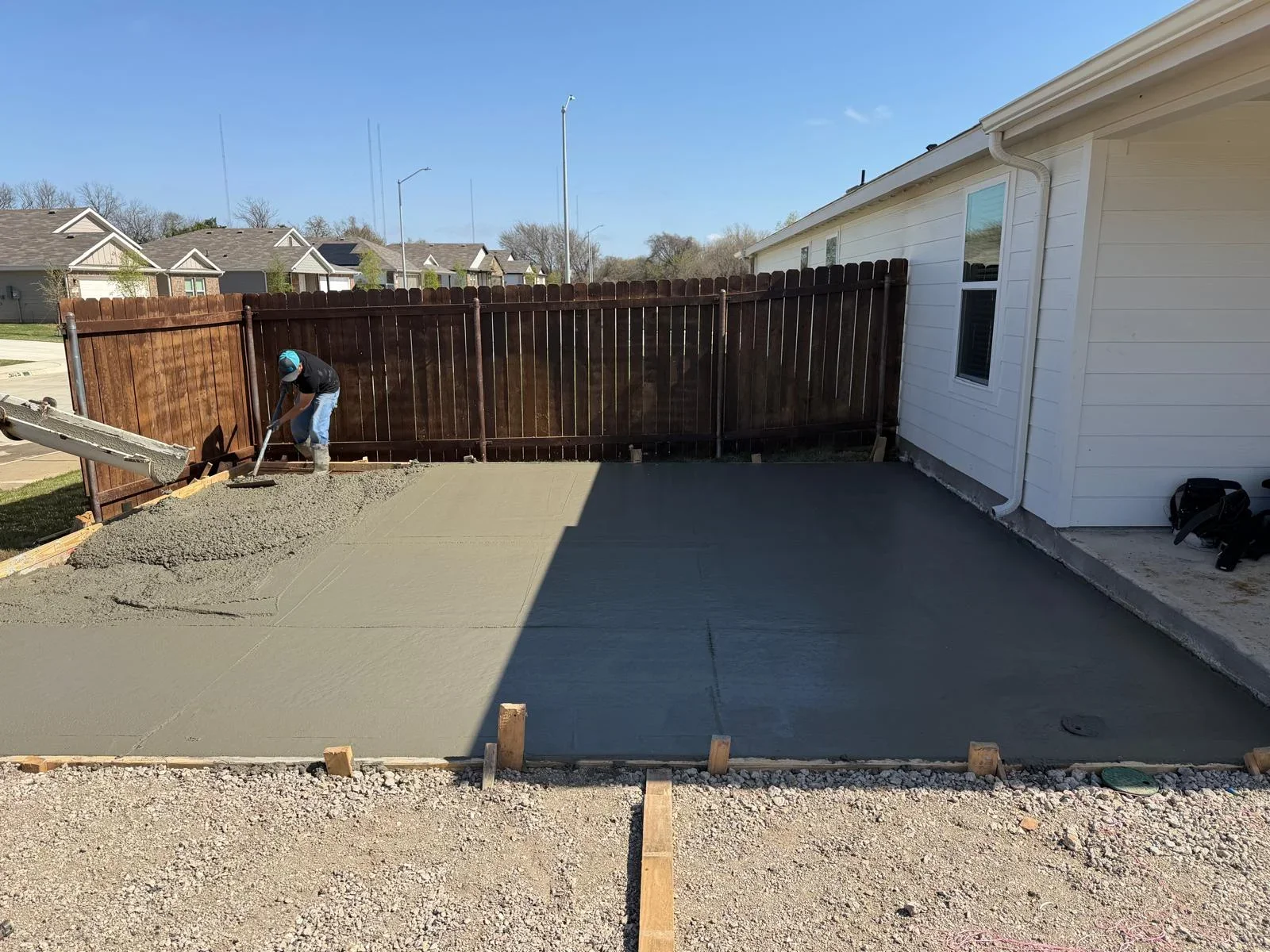 Worker finishing freshly poured concrete driveway with wooden forms and gravel base
