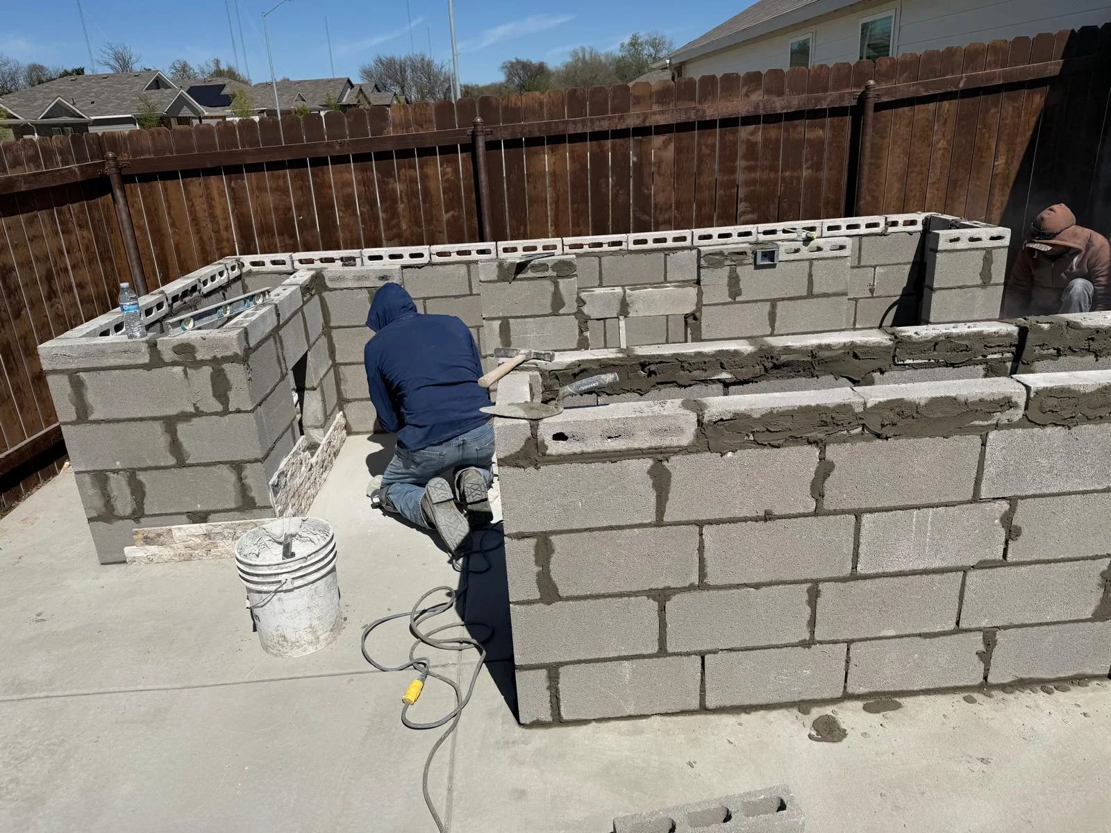 Concrete block retaining wall under construction with workers applying mortar and finishing masonry work
