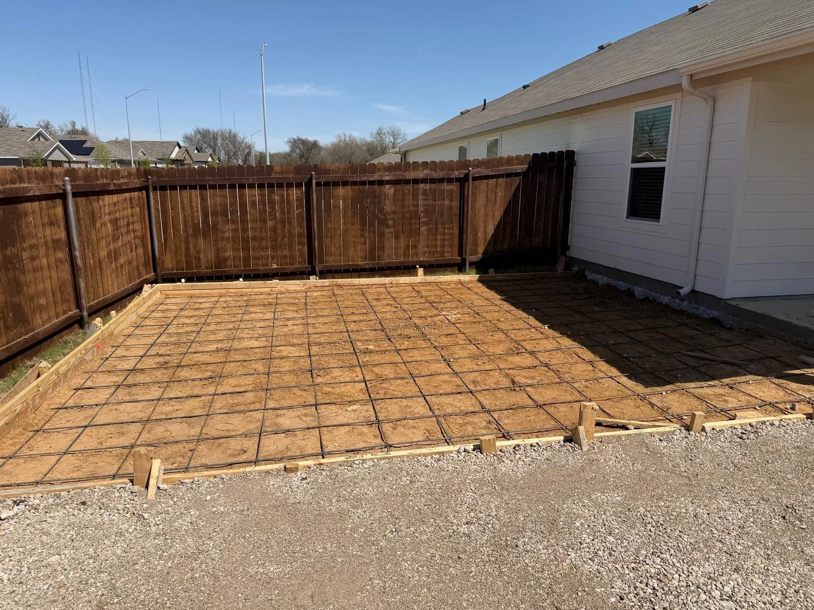 Concrete patio foundation with rebar grid and wooden forms in fenced backyard