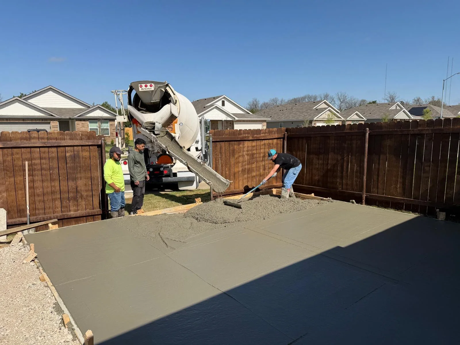 Concrete patio pour in progress with ready-mix truck and crew finishing concrete surface