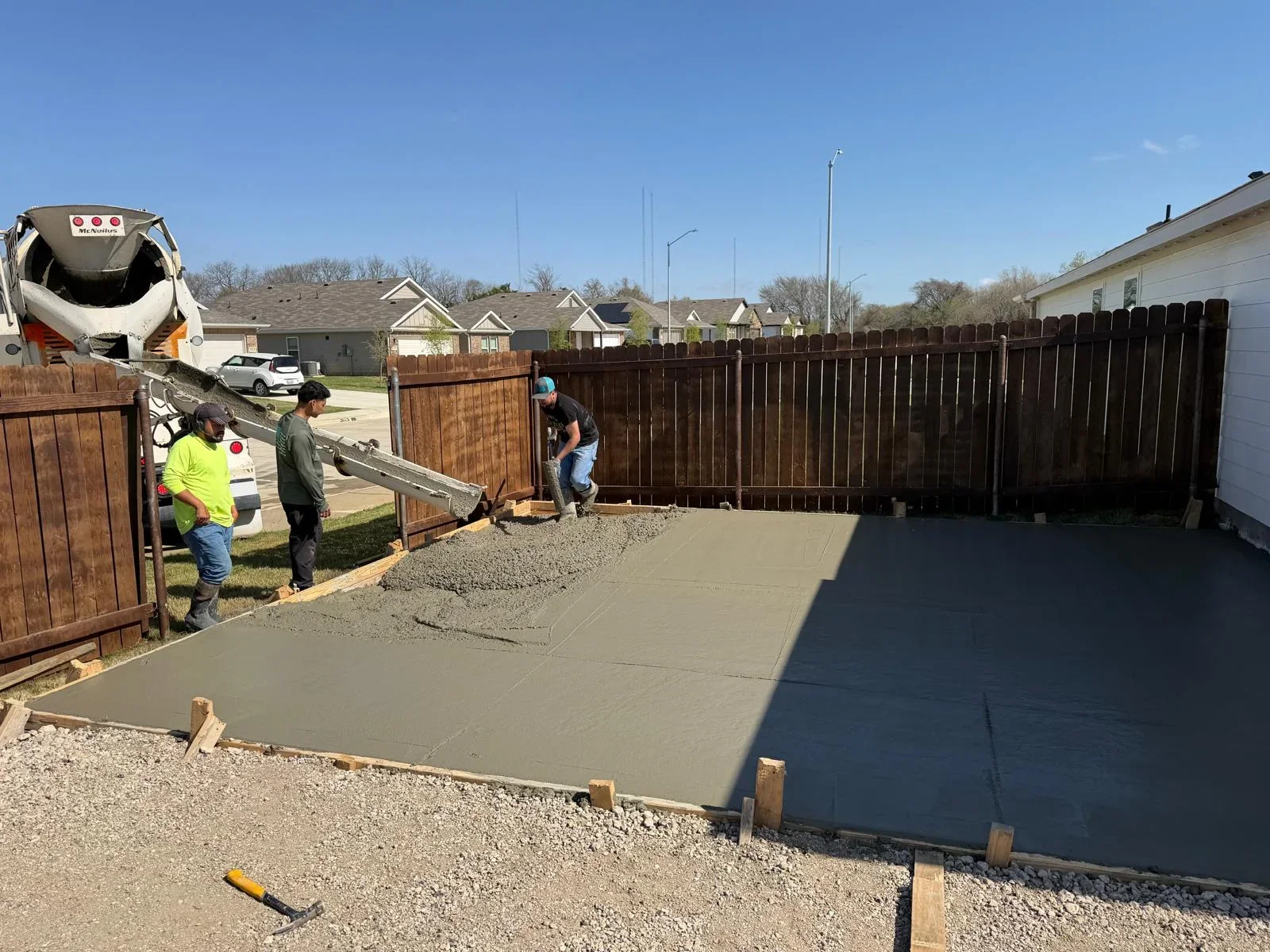 Concrete patio installation in progress with crew finishing surface and concrete truck on site