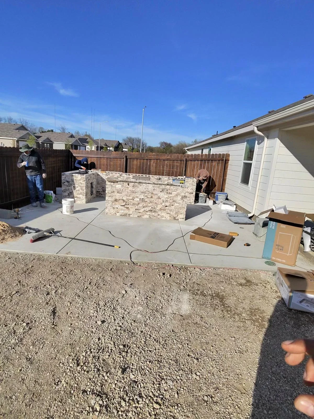 Concrete patio foundation with stone veneer structure under construction in residential backyard